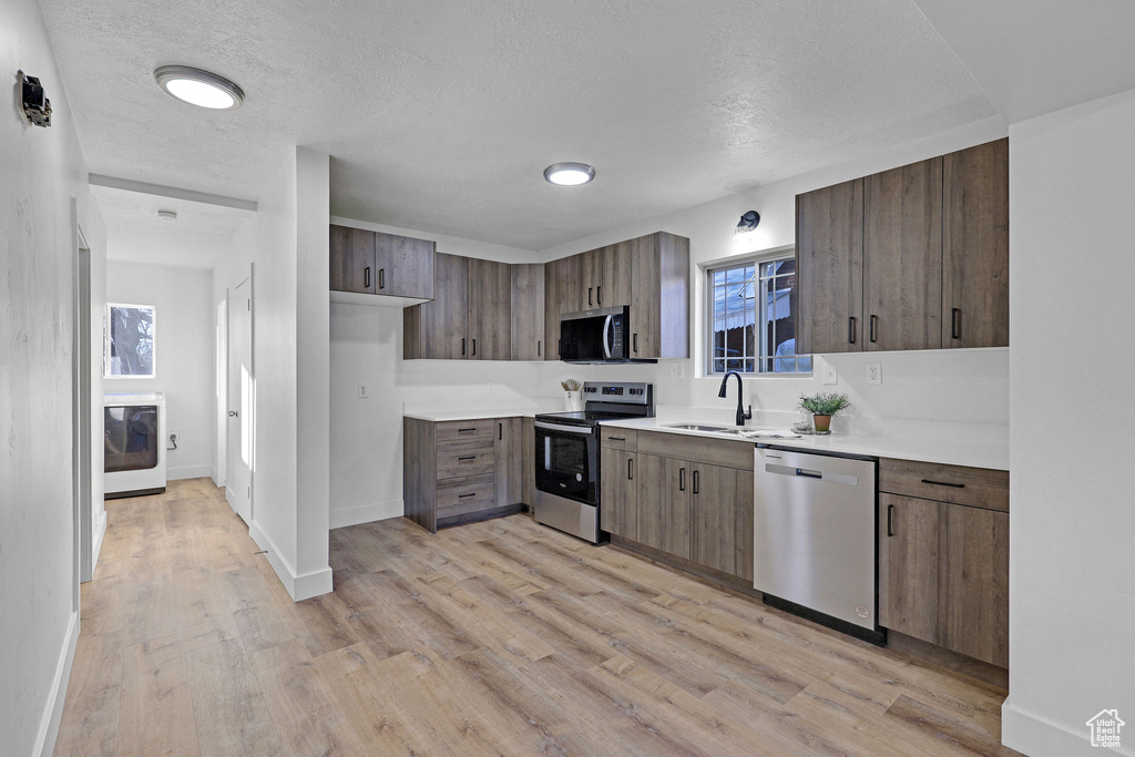 Kitchen with light hardwood / wood-style flooring, washer / dryer, sink, appliances with stainless steel finishes, and a textured ceiling