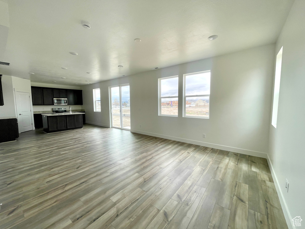 Unfurnished living room with light wood-style flooring, a sink, baseboards, and visible vents