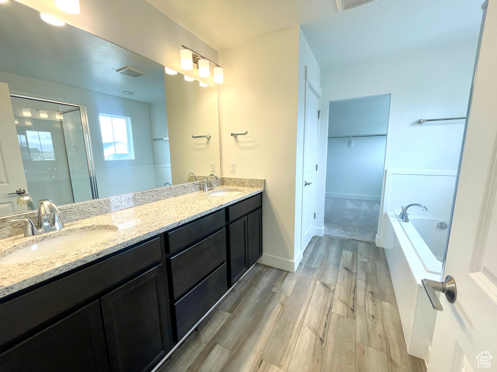 Bathroom featuring a shower stall, a sink, a garden tub, double vanity, and wood finished floors