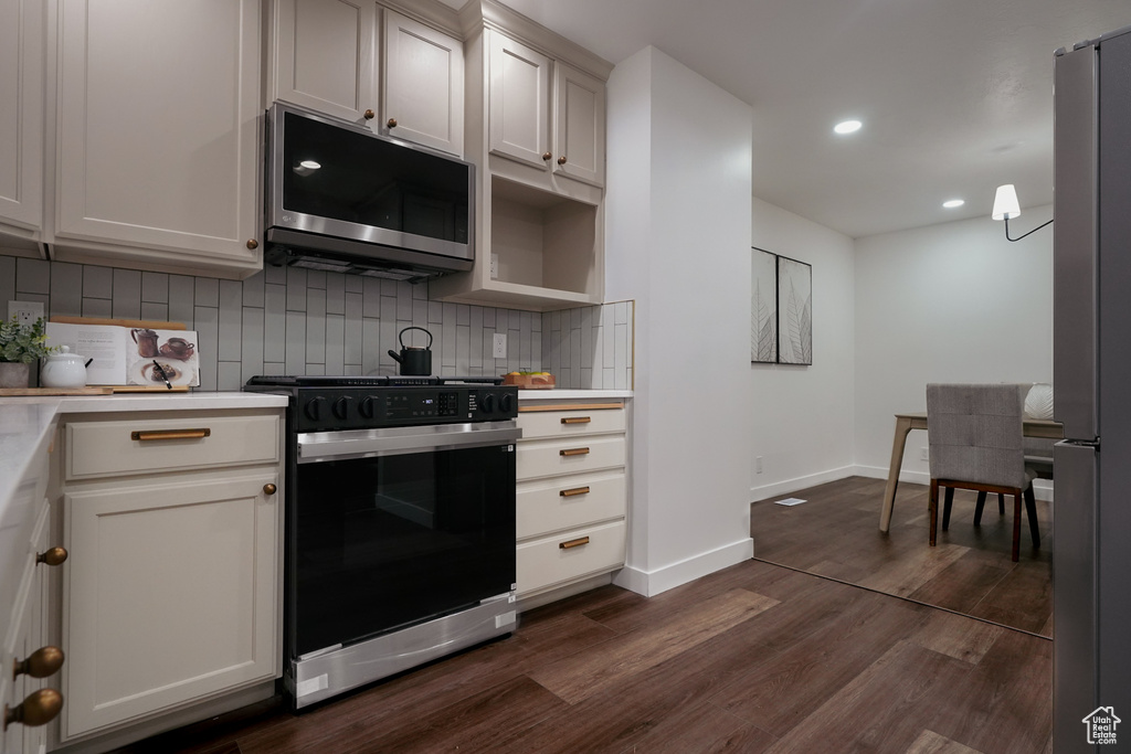 Kitchen featuring white cabinets, backsplash, hanging light fixtures, stainless steel appliances, and dark wood-type flooring