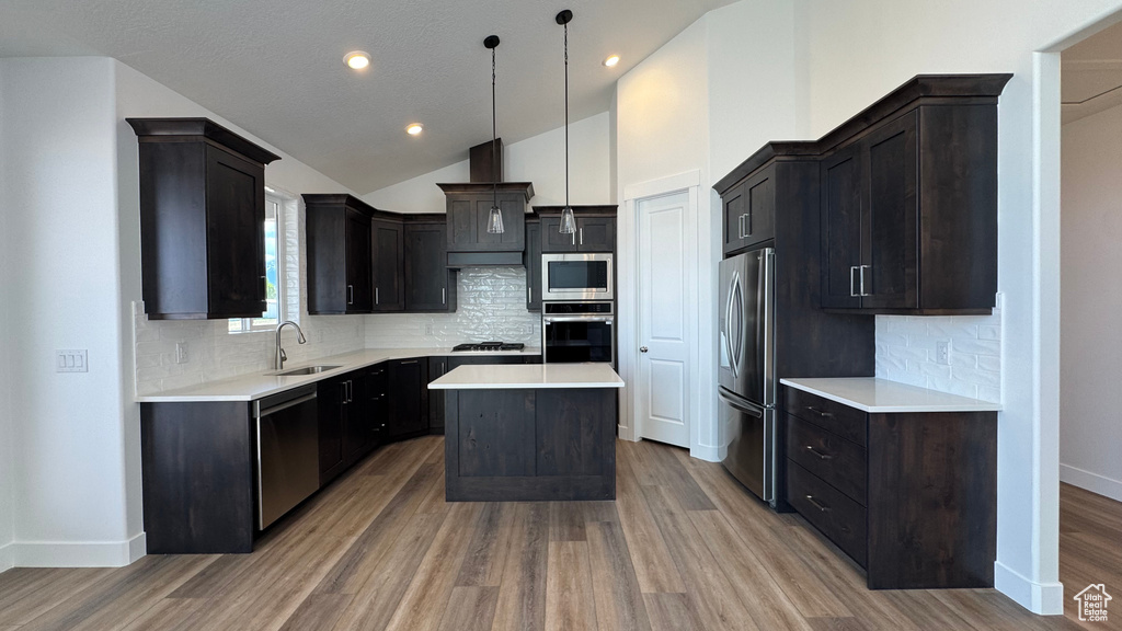 Kitchen featuring stainless steel appliances, a sink, light wood-type flooring, custom exhaust hood, and lofted ceiling