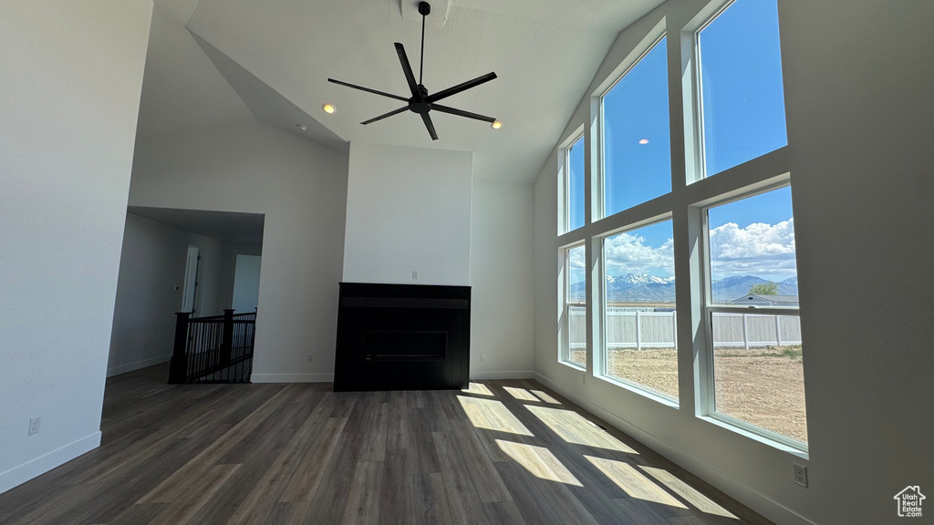Unfurnished living room featuring high vaulted ceiling, healthy amount of natural light, wood finished floors, and baseboards