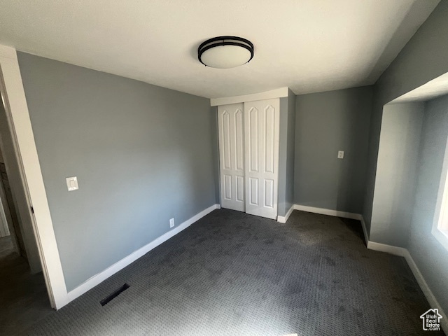 Unfurnished bedroom featuring dark carpet and a closet