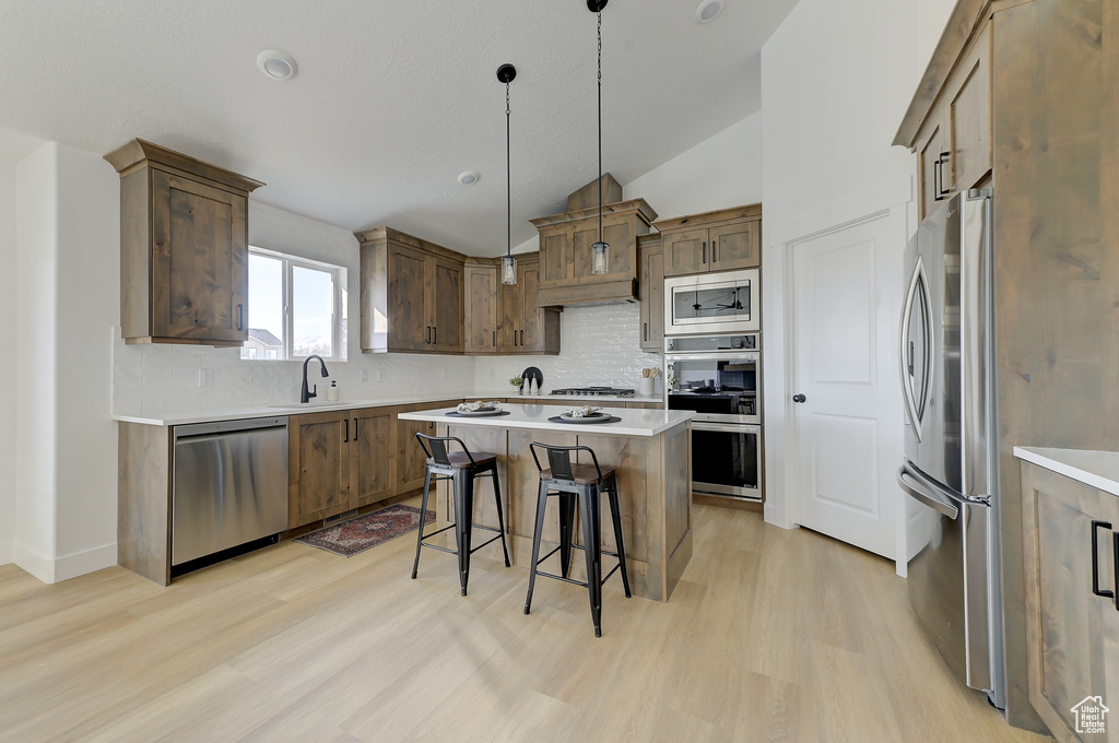 Kitchen with stainless steel appliances, decorative light fixtures, a breakfast bar, a center island, and sink