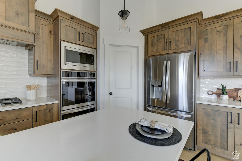 Kitchen with appliances with stainless steel finishes, hanging light fixtures, and decorative backsplash