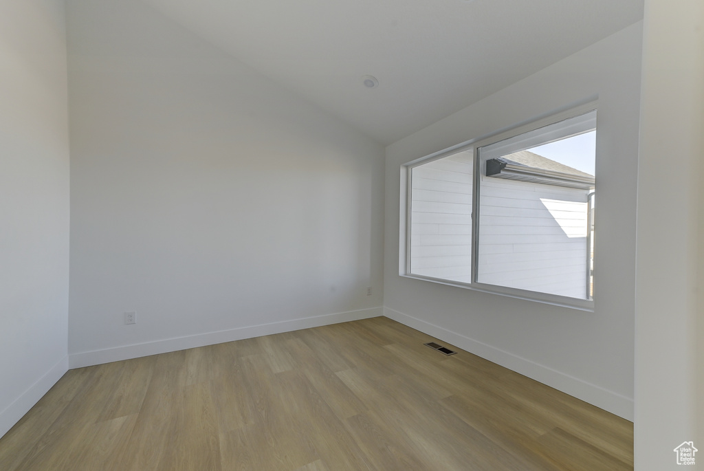 Spare room featuring light wood-type flooring and vaulted ceiling