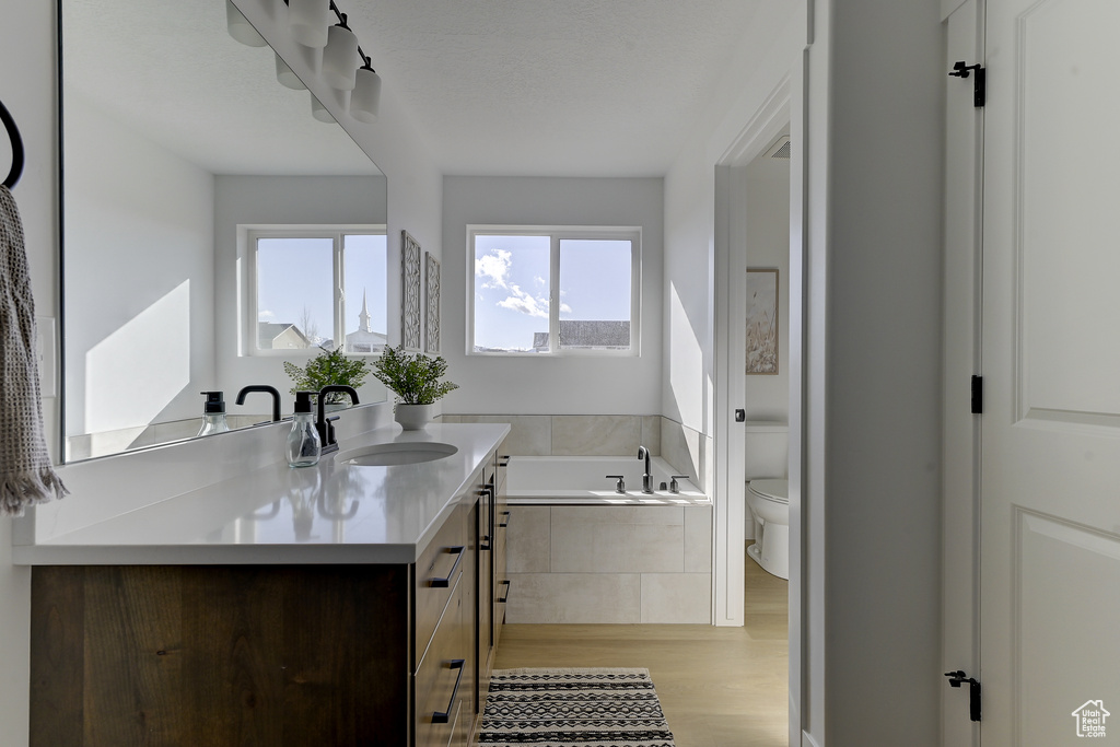 Bathroom with wood-type flooring, tiled tub, vanity, and toilet