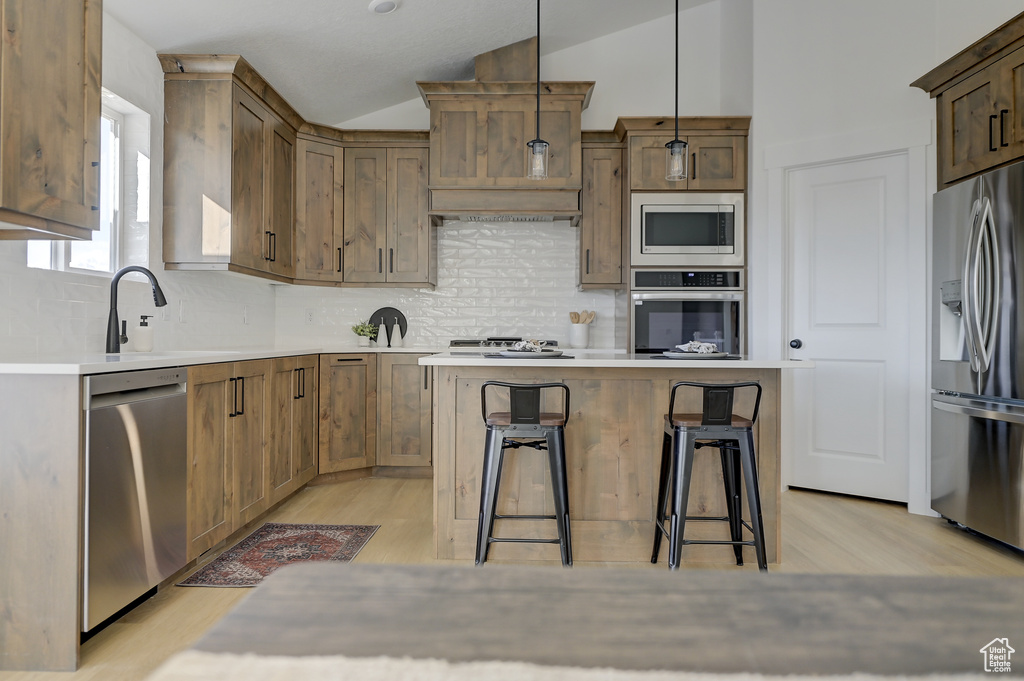 Kitchen with lofted ceiling, hanging light fixtures, light hardwood / wood-style floors, appliances with stainless steel finishes, and a kitchen breakfast bar