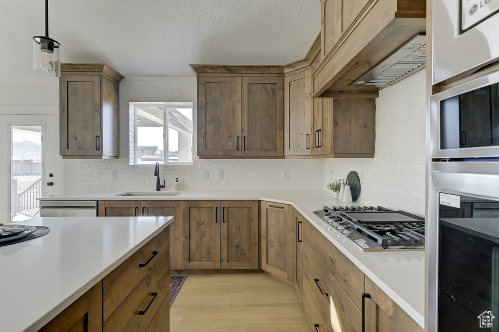 Kitchen featuring light hardwood / wood-style flooring, sink, decorative light fixtures, white dishwasher, and stainless steel gas cooktop