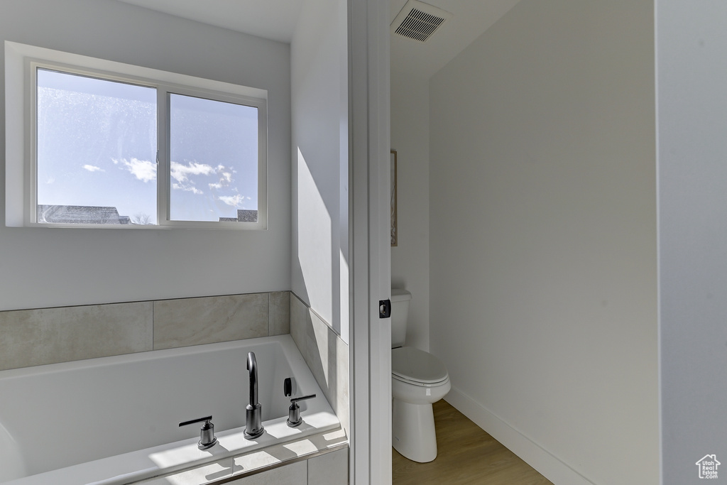 Bathroom featuring hardwood / wood-style flooring, tiled bath, toilet, and a healthy amount of sunlight