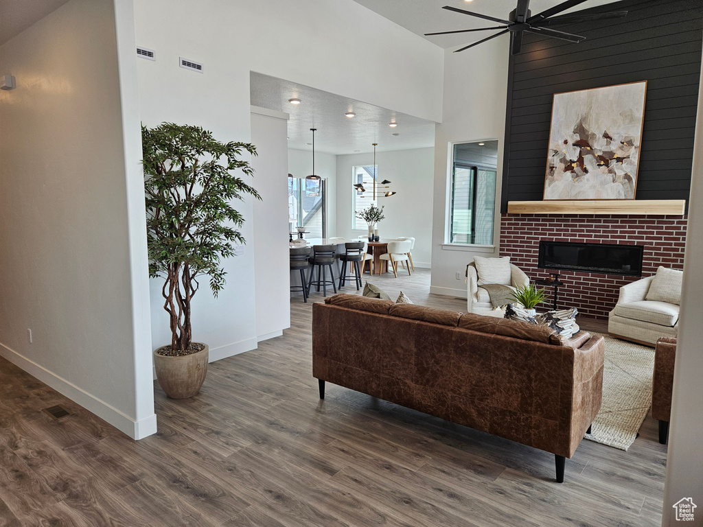 Living area featuring a ceiling fan, wood finished floors, baseboards, a fireplace, and a towering ceiling