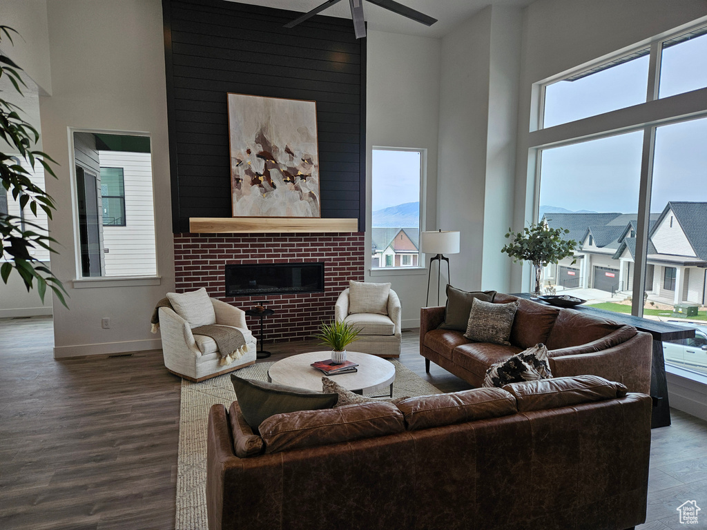Living area with a towering ceiling, plenty of natural light, wood finished floors, a ceiling fan, and a fireplace