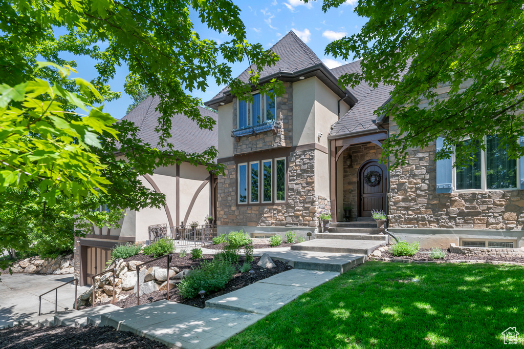 Tudor-style house featuring stone siding, stucco siding, a front yard, and a shingled roof