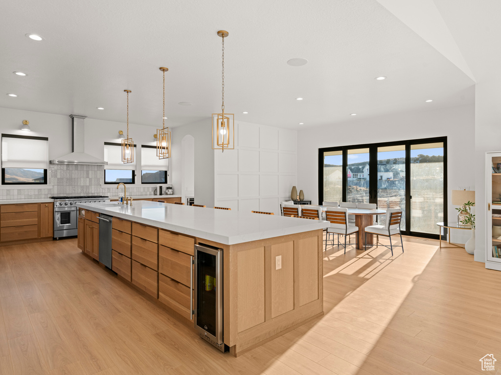 Kitchen featuring a large island, appliances with stainless steel finishes, hanging light fixtures, wine cooler, and wall chimney exhaust hood