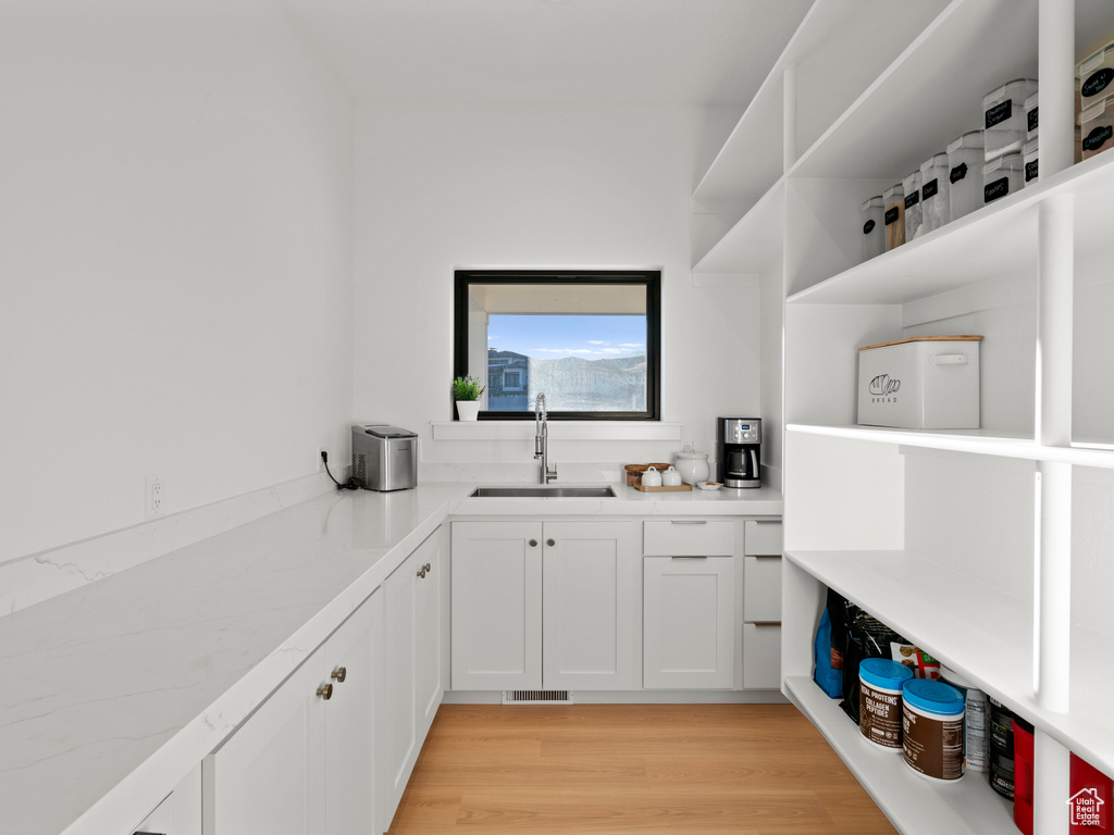 Interior space with white cabinetry, light stone counters, sink, and light hardwood / wood-style flooring