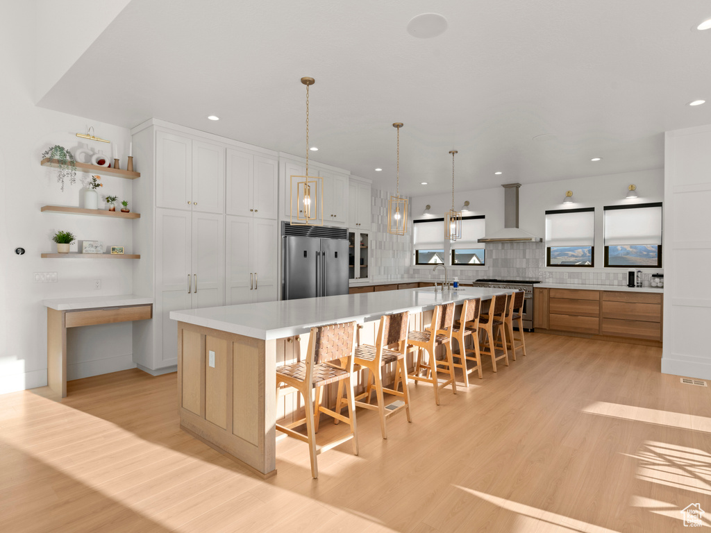 Kitchen featuring a breakfast bar, a large island with sink, high quality appliances, wall chimney range hood, and white cabinets