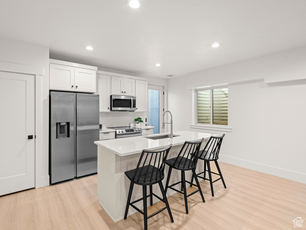 Kitchen featuring sink, an island with sink, stainless steel appliances, light hardwood / wood-style floors, and white cabinets