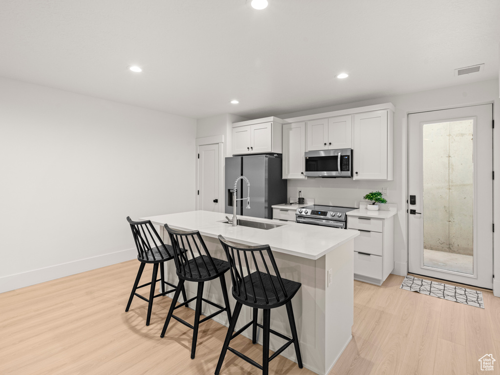 Kitchen featuring a kitchen bar, sink, white cabinetry, appliances with stainless steel finishes, and an island with sink