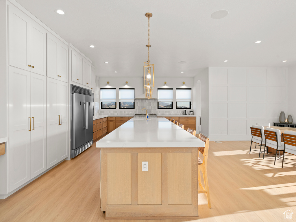 Kitchen featuring a spacious island, white cabinetry, stainless steel built in fridge, pendant lighting, and light hardwood / wood-style floors