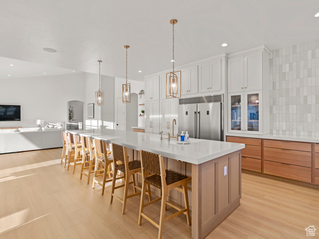 Kitchen with built in fridge, sink, white cabinets, hanging light fixtures, and a spacious island