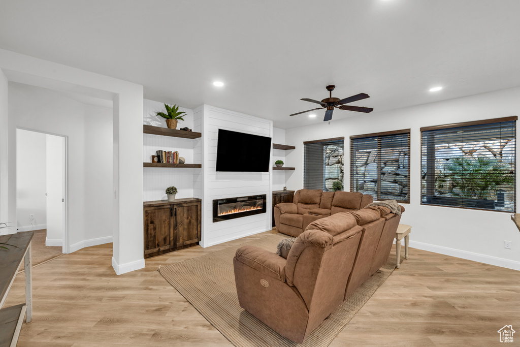 Living room with a fireplace, built in features, light hardwood / wood-style floors, and ceiling fan