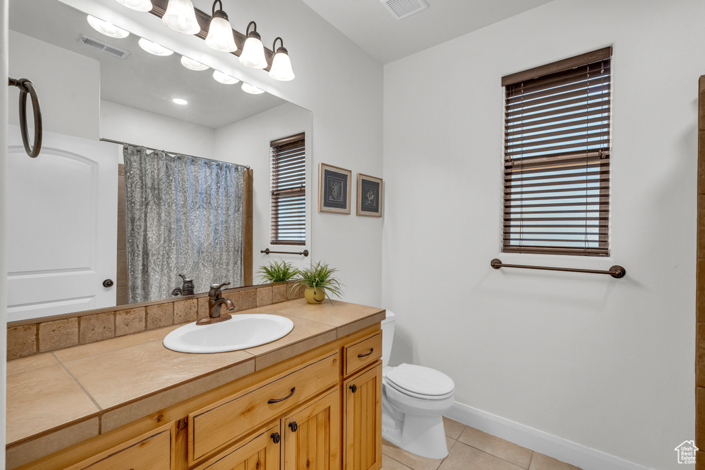 Bathroom with curtained shower, toilet, vanity, and tile patterned flooring