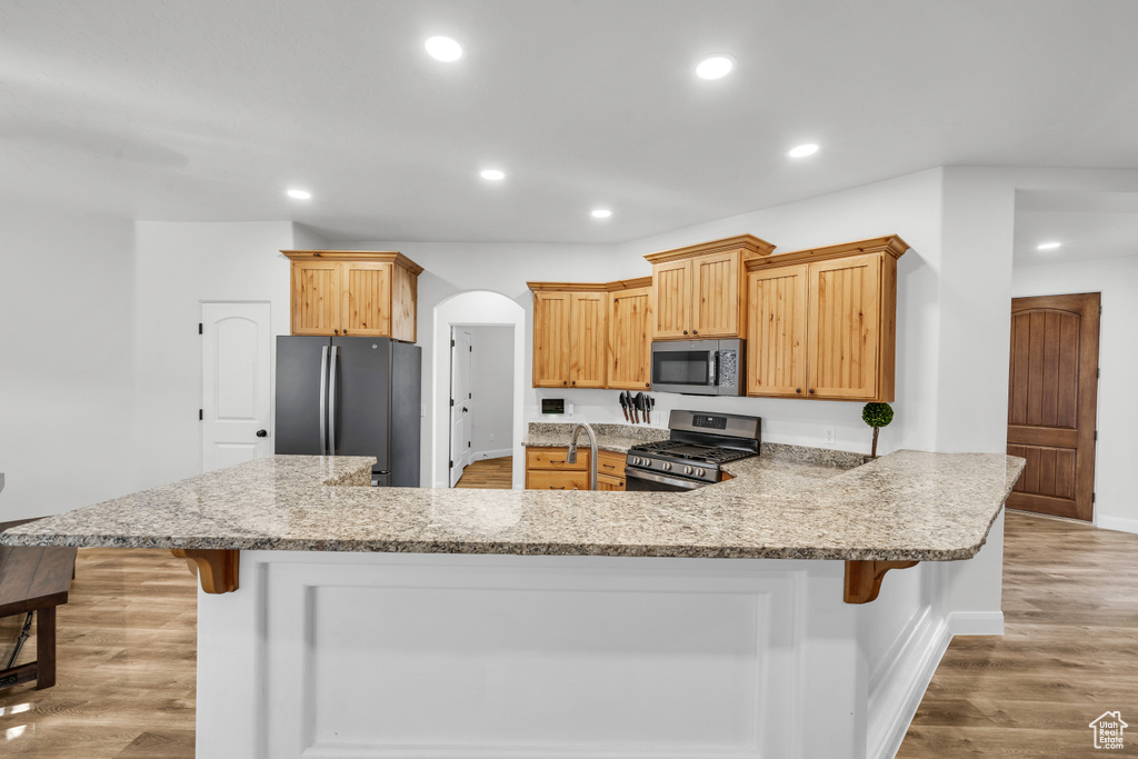 Kitchen featuring stainless steel appliances, a breakfast bar, light hardwood / wood-style floors, and kitchen peninsula