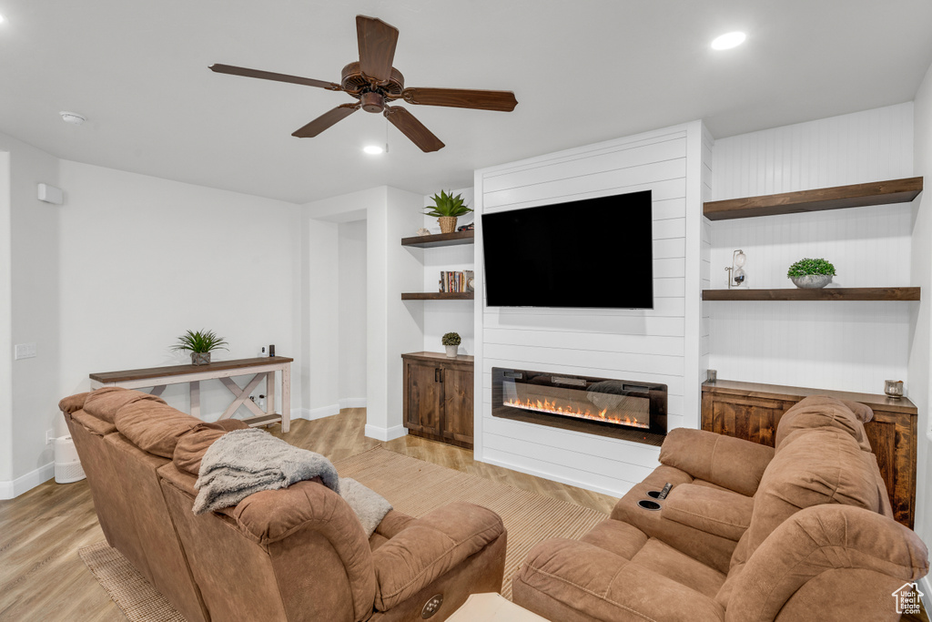 Living room with a large fireplace, ceiling fan, and light hardwood / wood-style flooring