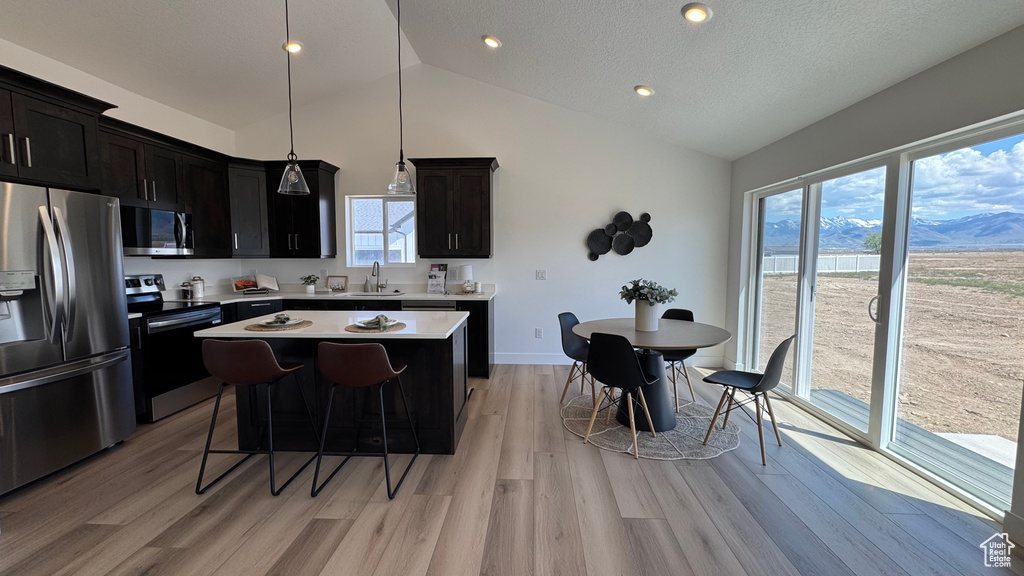Kitchen featuring appliances with stainless steel finishes, a sink, light wood-style flooring, a center island, and light countertops