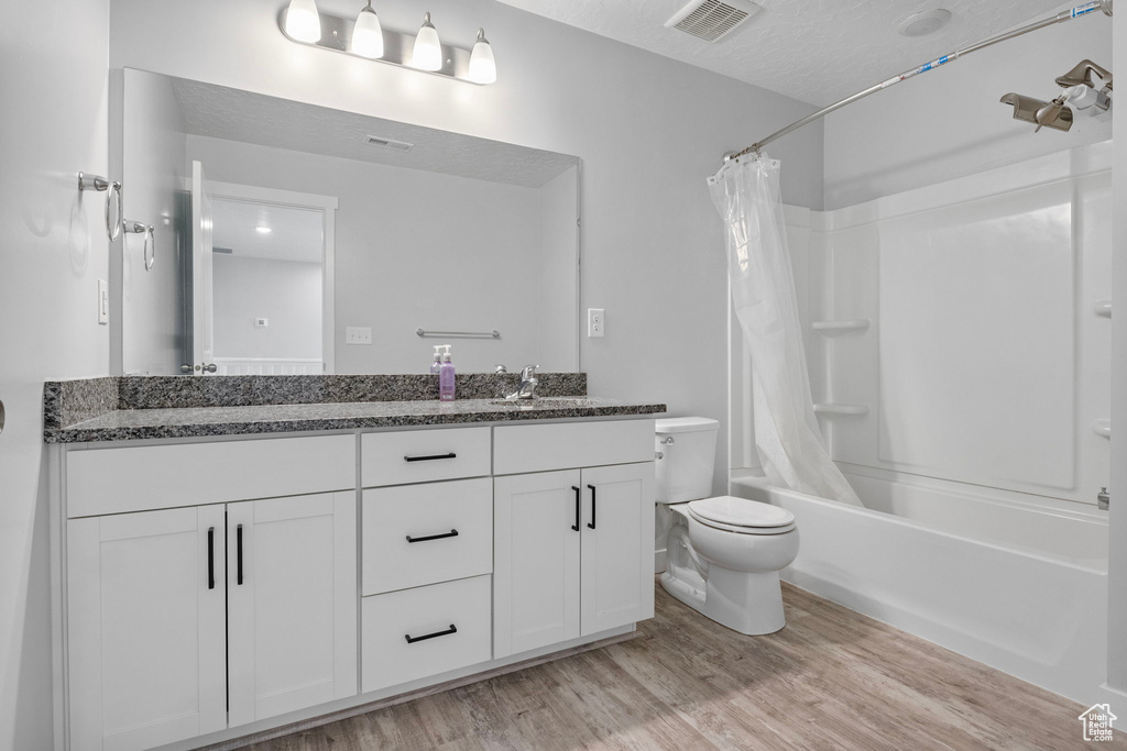 Full bathroom with toilet, a textured ceiling, vanity, shower / bath combo, and hardwood / wood-style floors