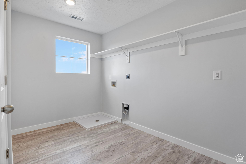 Laundry area with light hardwood / wood-style flooring, hookup for a washing machine, a textured ceiling, and electric dryer hookup