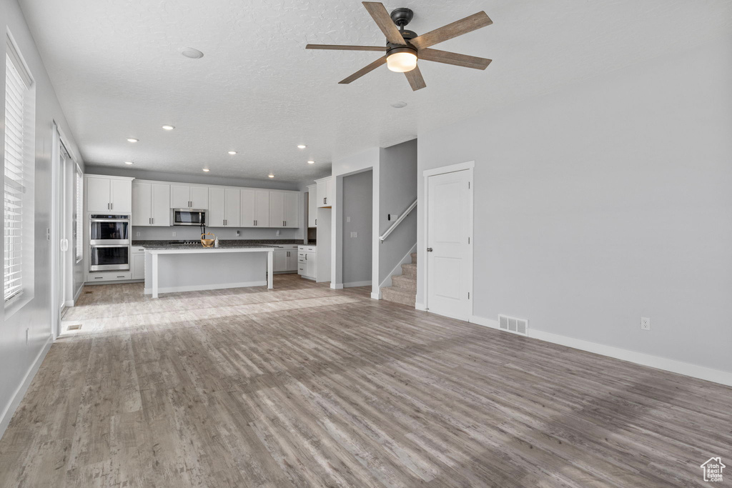 Unfurnished living room with a textured ceiling, ceiling fan, and light wood-type flooring