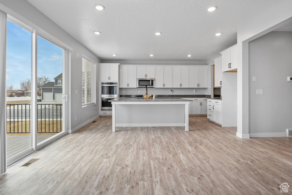 Kitchen featuring appliances with stainless steel finishes, an island with sink, light wood-type flooring, white cabinets, and a textured ceiling