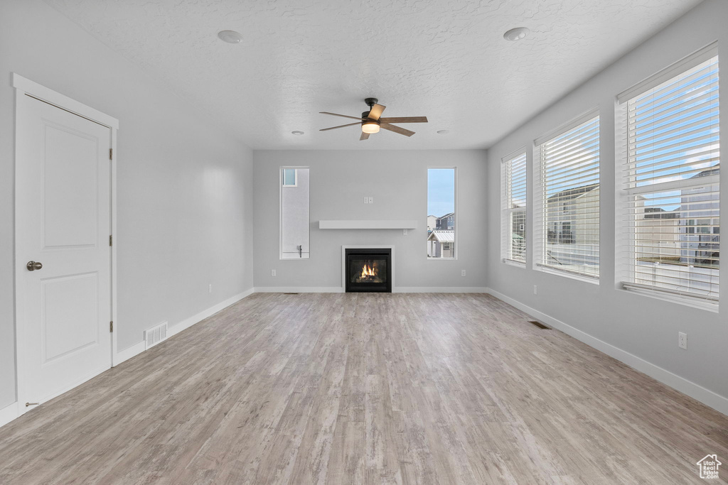 Unfurnished living room with ceiling fan, a textured ceiling, and light wood-type flooring