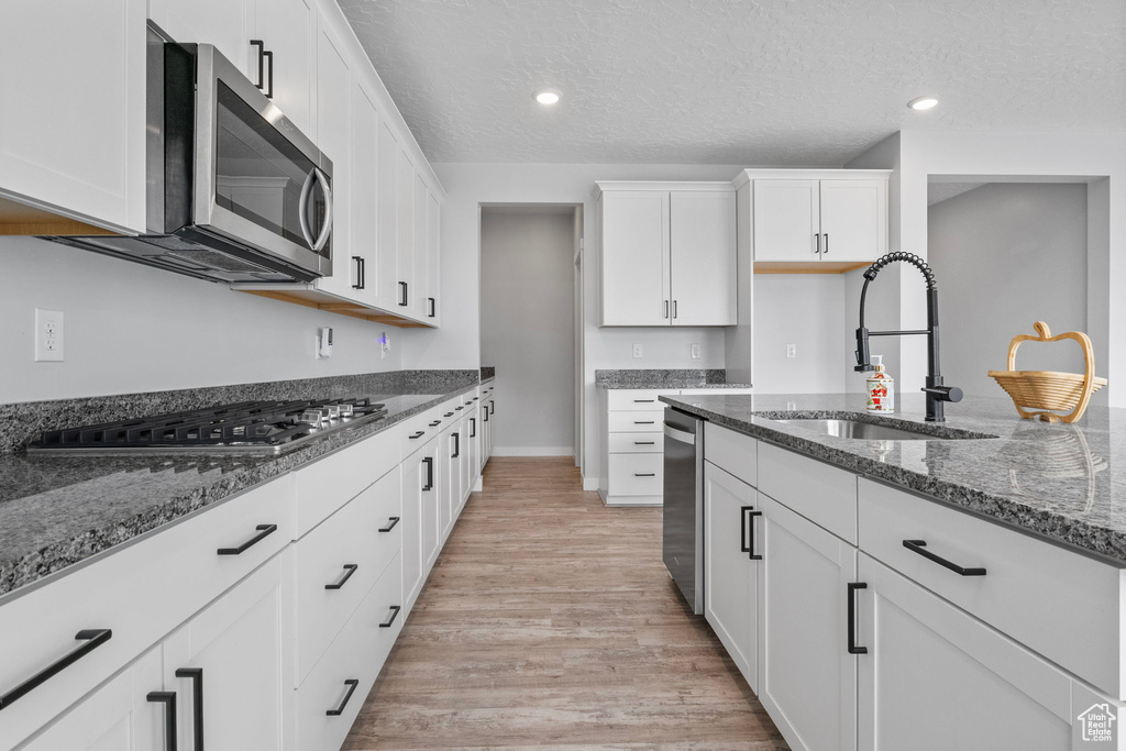 Kitchen with stainless steel appliances, sink, white cabinets, and dark stone counters