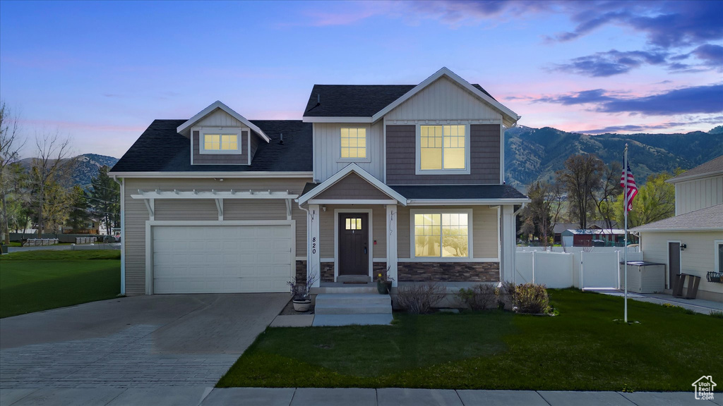 Craftsman-style home with fence, stone siding, a mountain view, concrete driveway, and a yard