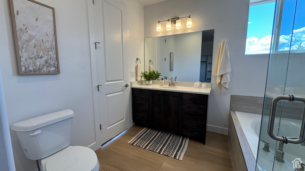 Full bathroom with wood finished floors, toilet, tiled bath, vanity, and baseboards