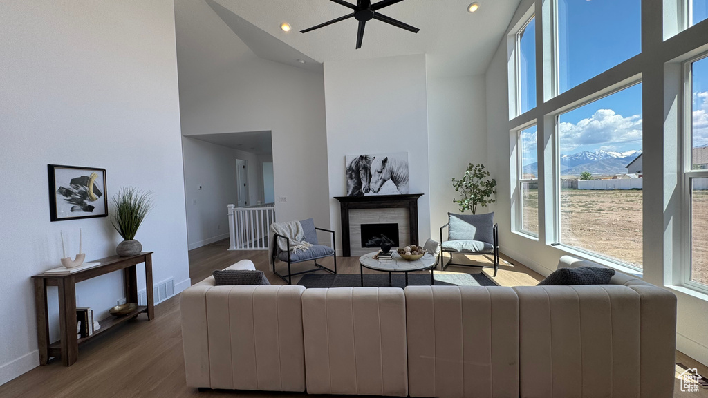 Living room featuring high vaulted ceiling, plenty of natural light, a fireplace, wood finished floors, and ceiling fan