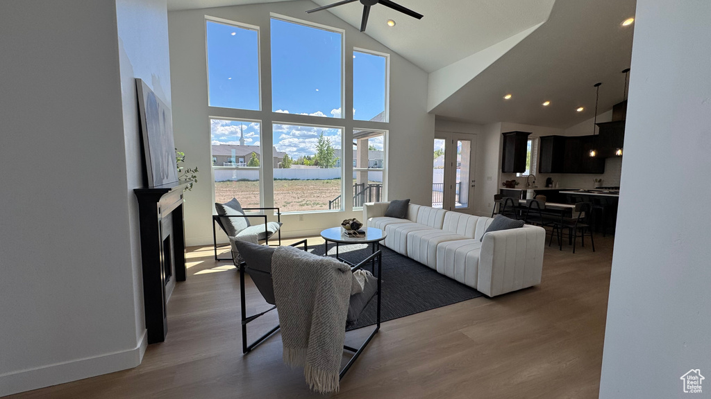Living area with ceiling fan, high vaulted ceiling, wood finished floors, recessed lighting, and a water view