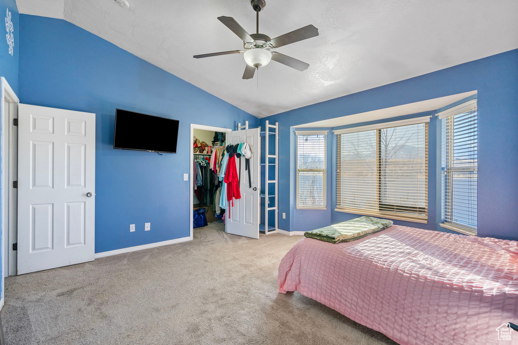 Unfurnished bedroom with ceiling fan, a spacious closet, vaulted ceiling, light colored carpet, and a closet