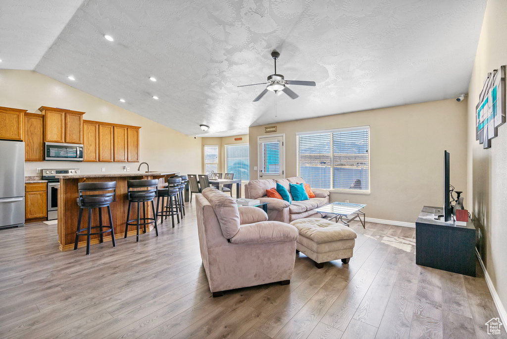 Living room with ceiling fan, lofted ceiling, light hardwood / wood-style flooring, and a textured ceiling