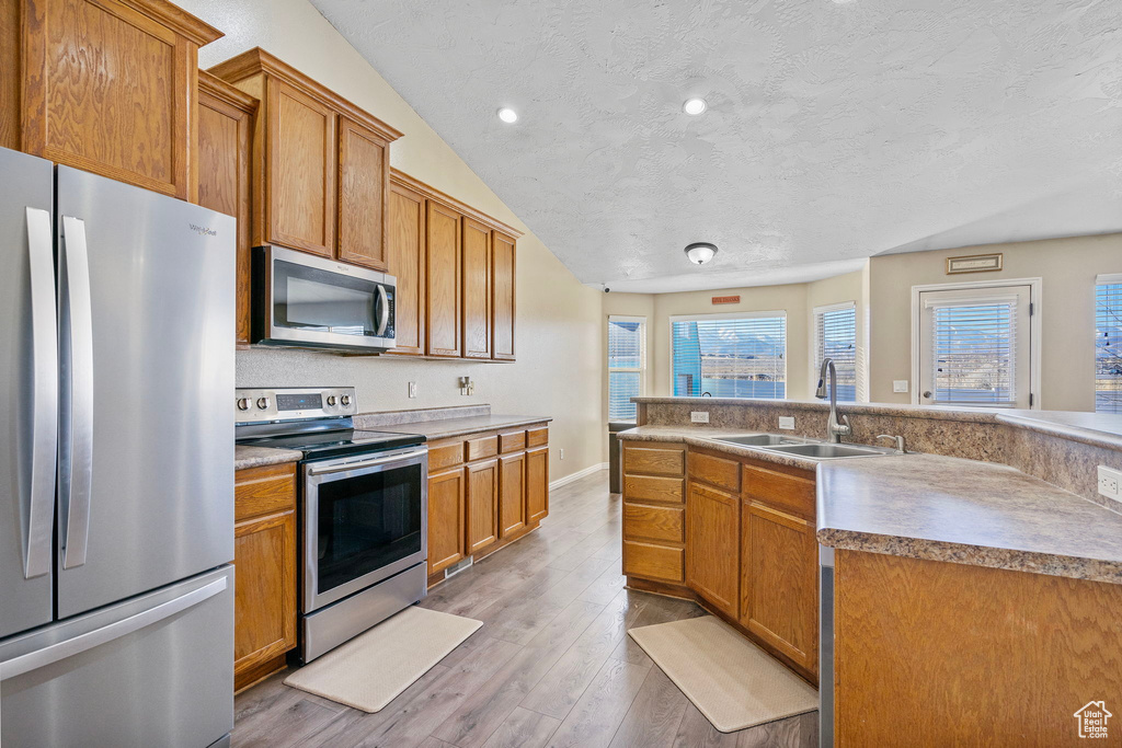 Kitchen with sink, a textured ceiling, an island with sink, hardwood / wood-style flooring, and stainless steel appliances