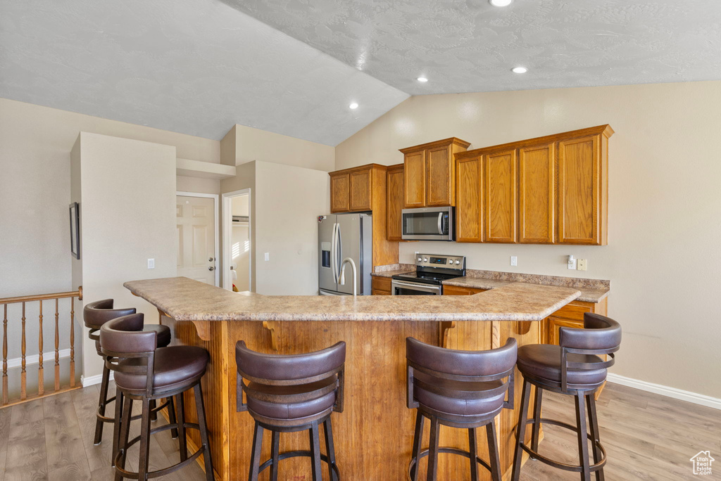 Kitchen featuring stainless steel appliances, vaulted ceiling, a breakfast bar area, and light hardwood / wood-style floors