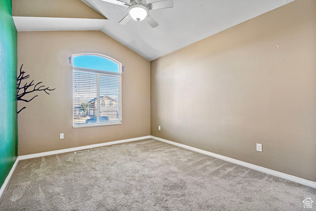 Carpeted empty room featuring ceiling fan and vaulted ceiling