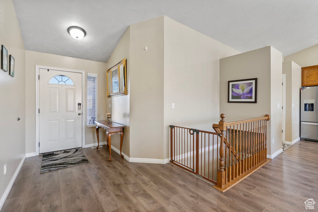 Foyer entrance with wood-type flooring and vaulted ceiling