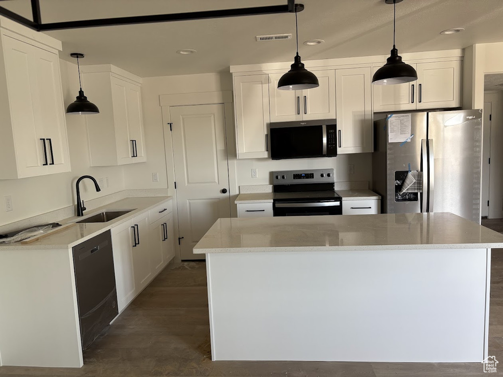 Kitchen featuring appliances with stainless steel finishes, a center island, pendant lighting, and white cabinets