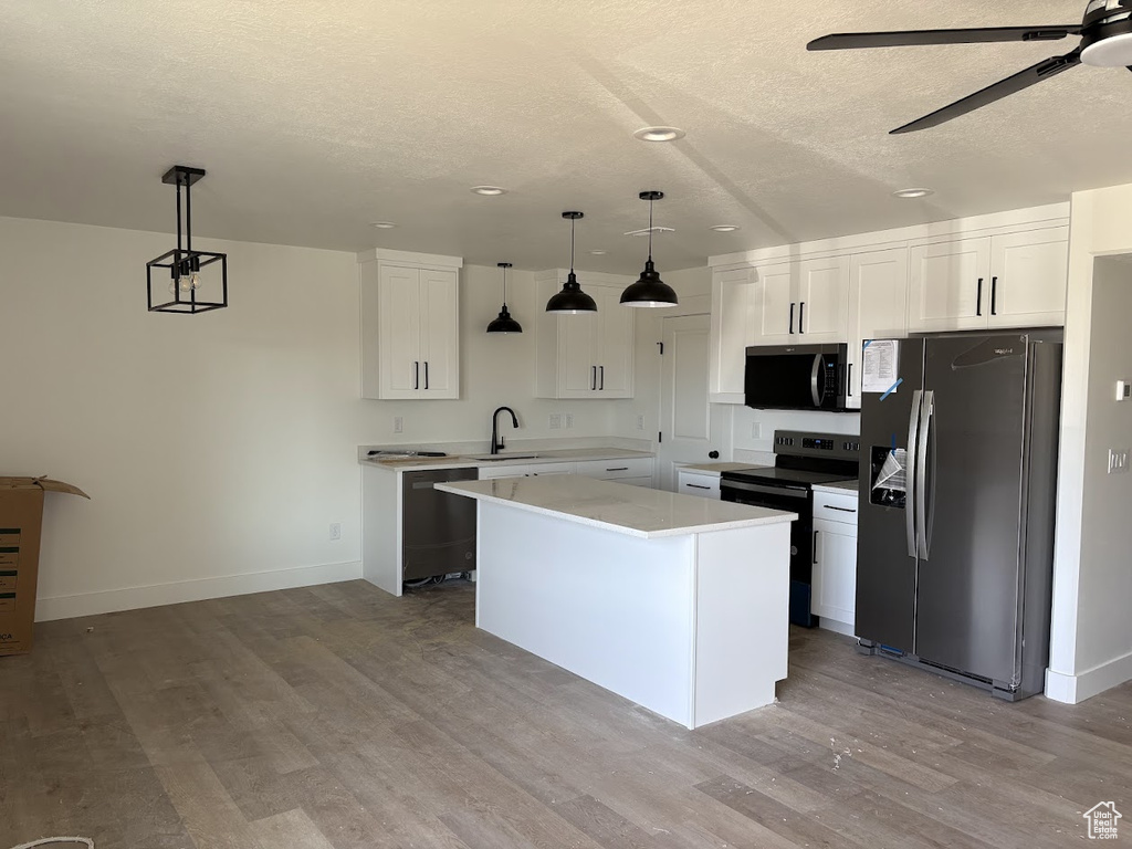 Kitchen with white cabinets, decorative light fixtures, a kitchen island, and black appliances