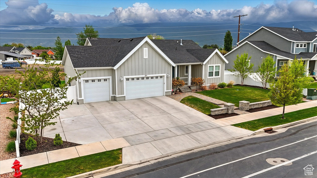 Ranch-style house featuring an attached garage, fence, driveway, board and batten siding, and roof with shingles