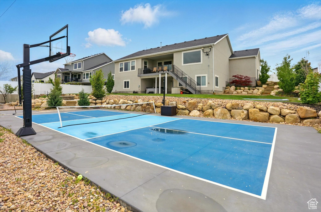 View of basketball court featuring basketball hoop, stairway, a tennis court, and fence