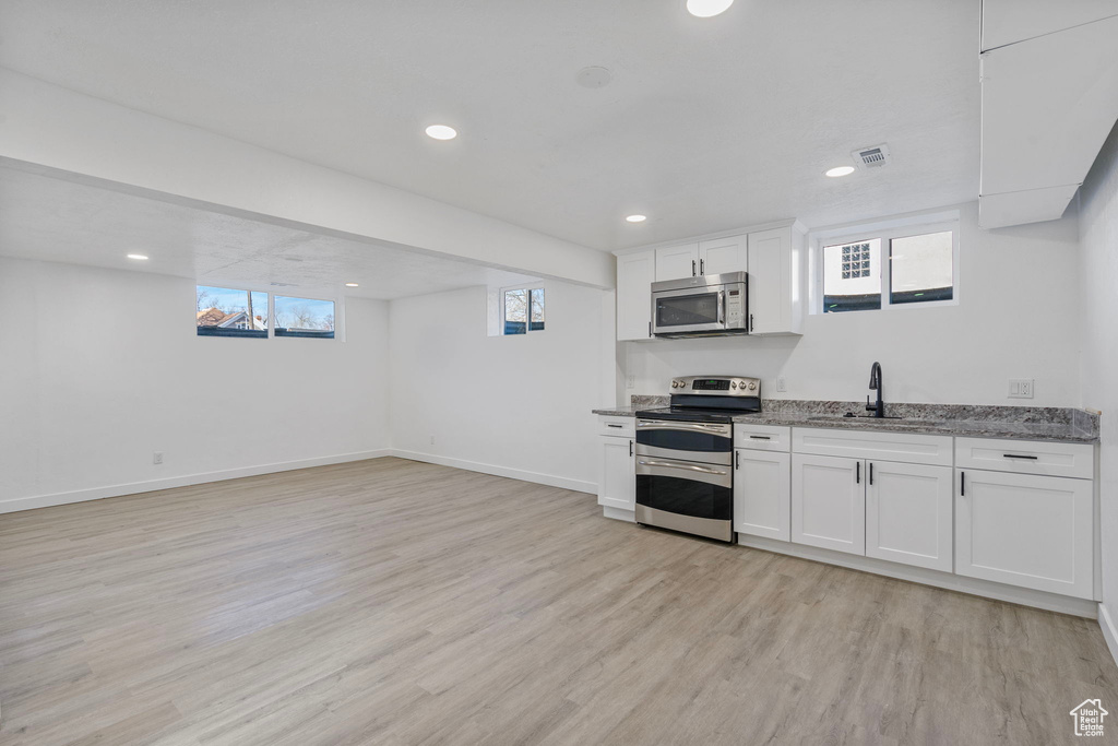 Kitchen featuring stainless steel appliances, light stone countertops, light hardwood / wood-style flooring, and white cabinets